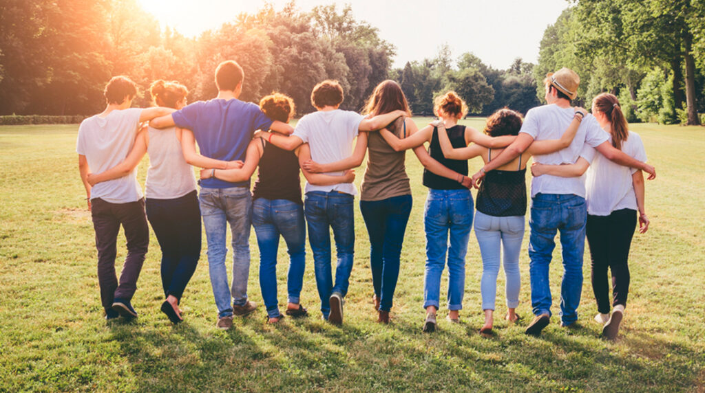 A community group walking through a green field, arm in arm.